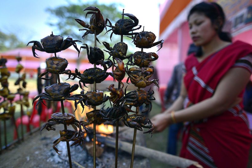 Kamrup, 2017. február 3. Pálcákra tűzött füstölt rákokat kínál egy utcai árus a Szagraszal fesztiválon az északkelet-indiai Asszám állambeli Kamrupban 2017. február 3-án. Az ünnepségen a tiva (Tiwa) törzs tagjai tyúkokat áldoznak, a fiatalok pedig táncot lejtenek a bőséges termésért. A szövetségi államban nagy arányban élő, lalung néven is ismert tiva népcsoport a talaj pihentetése végett parlagoló rendszerben váltogatja a művelés alá vont földterületeit. (MTI/EPA)