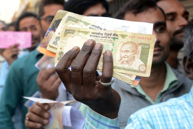 An Indian man holds up money to be exchanged as people wait in a queue to deposit and exchange 500 and 1000 rupee notes outside a bank in Amritsar on November 16, 2016. Long queues formed outside banks in India since the government's shock decision to withdraw the two largest denomination notes from circulation. / AFP PHOTO / NARINDER NANU