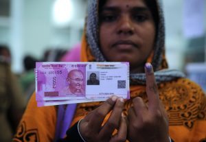 A Indian woman poses with new 2000 rupee notes, her Aadhaar ID card and a finger inked with indelible ink after exchanging withdrawn 500 and 1000 rupee banknotes at a bank in Chennai on November 17, 2016. India is to use indelible ink to prevent people from exchanging old notes more than once, the government said November 15, a week after the withdrawal of high-value banknotes from circulation in a crackdown on "black money". / AFP PHOTO / ARUN SANKAR