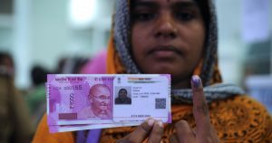 A Indian woman poses with new 2000 rupee notes, her Aadhaar ID card and a finger inked with indelible ink after exchanging withdrawn 500 and 1000 rupee banknotes at a bank in Chennai on November 17, 2016. India is to use indelible ink to prevent people from exchanging old notes more than once, the government said November 15, a week after the withdrawal of high-value banknotes from circulation in a crackdown on "black money". / AFP PHOTO / ARUN SANKAR