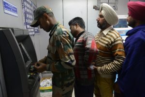 An Indian army soldier withdraws money at the front of a queue from an ATM in Amritsar on November 17, 2016. Long queues formed outside banks in India since the government's shock decision to withdraw the two largest denomination notes from circulation. / AFP PHOTO / NARINDER NANU
