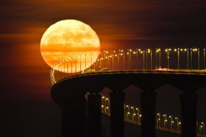 A full moon rising over the Re Island Bridge in Rivedoux is pictured on December 14, 2016. / AFP PHOTO / Xavier LEOTY