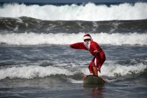 A surfer dressed in a Santa Claus outfit surfs on Kuta beach on Indonesia's resort island of Bali on December 19, 2016. The popular resort island, a pocket of Hindu culture in a country with the biggest Muslim population in the world, receives thousands of tourists every year over the Christmas season. / AFP PHOTO / SONNY TUMBELAKA