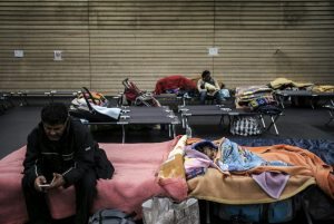 A man rests near his sleeping baby in a gymnasium where homeless people and families are housed, on January 5, 2017 in Lyon, central-eastern France, as measures of the French government's Cold Weather Plan (Plan Grand Froid) start to be applied in the region. / AFP PHOTO / JEFF PACHOUD