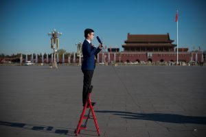 A television journalist stands on a ladder as he reports ahead of the CPPCC Closing ceremony at the Great Hall of the People in Beijing on March 13, 2017. More than 3000 delegates from across China are attending the annual meeting of the country's rubber-stamp congress. / AFP PHOTO / NICOLAS ASFOURI