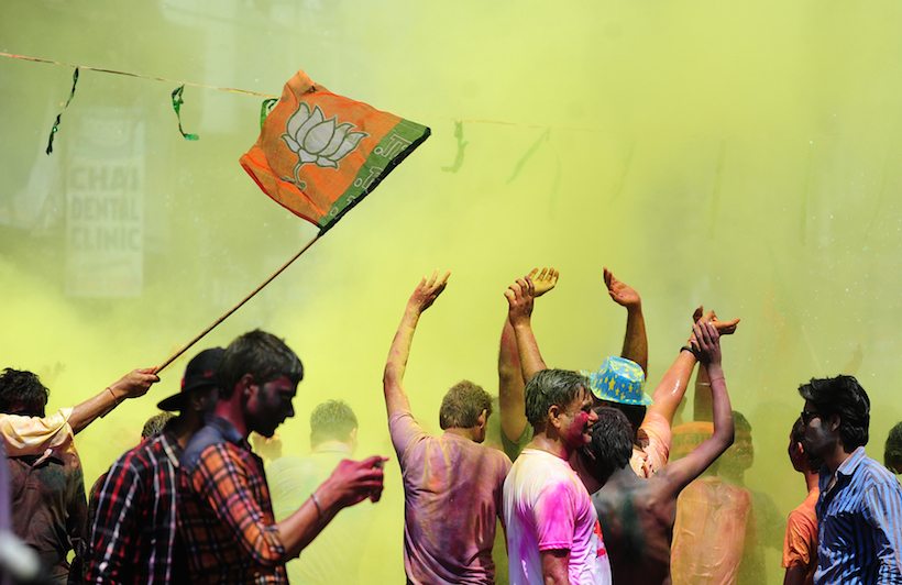 Indian people dance as they celebrate the Holi festival with a Bharatiya Janata Party (BJP) flag in Allahabad on March 13, 2017. Holi, the festival of colours, is a riotous celebration of the coming of spring and falls on the day after full moon annually in March. / AFP PHOTO / SANJAY KANOJIA