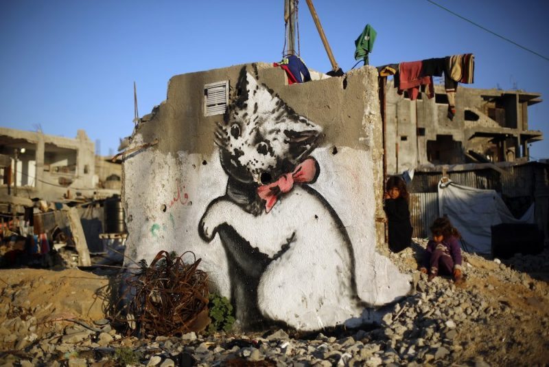 A Palestinian child stands next to a mural of a kitten, said to have been painted by British street artist Banksy, on the remains of a house that was destroyed during the 50-day war between Israel and Hamas militants in the summer of 2014, in the Gaza Strip town of Beit Hanun on February 26, 2015. AFP PHOTO / MOHAMMED ABED / AFP PHOTO / MOHAMMED ABED