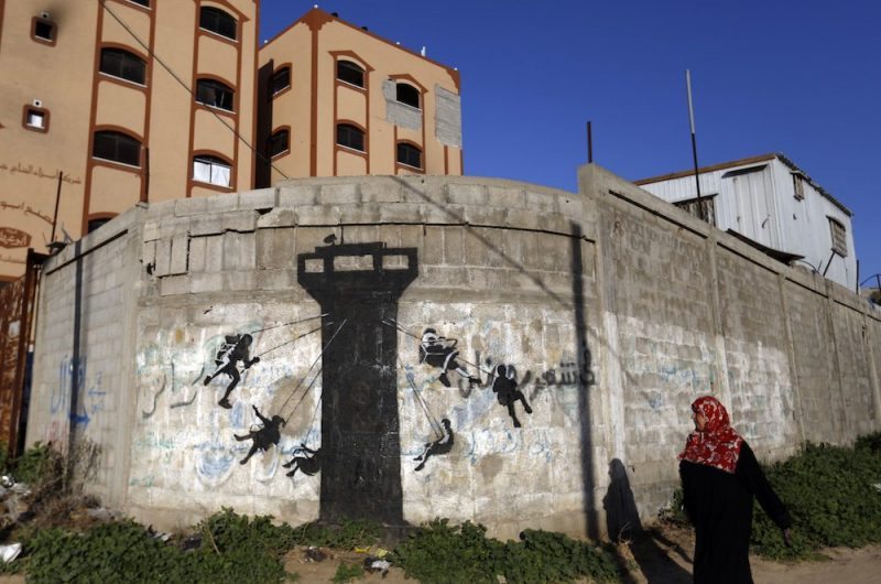 A Palestinian woman walks past a mural of children using an Israeli army watch tower as a swing ride, said to have been painted by British street artist Banksy, on the remains of a house that was destroyed during the 50-day war between Israel and Hamas militants in the summer of 2014, in the Gaza Strip town of Beit Hanun on February 26, 2015. AFP PHOTO / MOHAMMED ABED / AFP PHOTO / MOHAMMED ABED