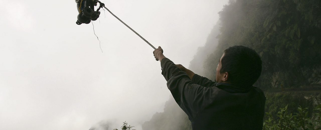 YUNGAS, BOLIVIA - DECEMBER 21: A member of a road crew holds onto a hook that will be used to pull-up a truck that recently went off a cliff on the road connecting the city of La Paz to the Coroico in the North Yungas December 21, 2005 in the Yungas, Bolivia. Referred to as the Worlds Most Dangerous Road (WMDR) by the Inter-American Development Bank, the road, a narrow dirt track, descends nearly 11,800 ft. in just 40 miles. With no other options currently available, vehicles are forced to drive it, resulting in hundreds of annual deaths as trucks, buses and passenger cars fall thousands of feet down. Bolivia, the poorest country in Latin America, has just elected Evo Morales as President, bringing a sense of hope that infrastructure and living conditions will finally improve. (Photo by Spencer Platt/Getty Images)