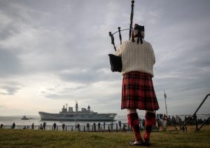 PORTSMOUTH, ENGLAND - DECEMBER 07: Piper Larry Cunningham plays his bagpipes as Britain's last serving aircraft carrier HMS Illustrious is towed from her home port at Portsmouth Docks after being sold for scrap on December 7, 2016 in Portsmouth, England. The 22,000 tonne ship, whose service started in 1982 in the aftermath of the Falklands War and saw deployments in Bosnia and Sierra Leone, was affectionately known as 'Lusty' and will be broken up for scrap in Turkey despite attempts last minute attempts to save her. (Photo by Matt Cardy/Getty Images)