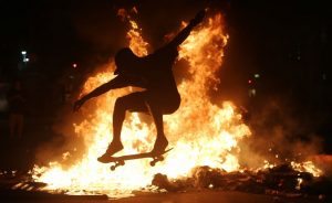 RIO DE JANEIRO, BRAZIL - MARCH 15: A young man practices a skateboarding move in front of a fire set by protestors following a demonstration against proposed federal government reforms on March 15, 2017 in Rio de Janeiro, Brazil. Protestors rallied nationwide, mostly peacefully, against proposed rules tightening pensions as the country continues to suffer through a financial and political crisis. (Photo by Mario Tama/Getty Images)